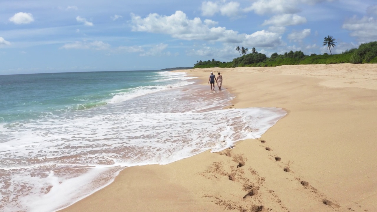 一对情侣走在原始的沙滩上，海浪抚摸着他们的脚视频素材