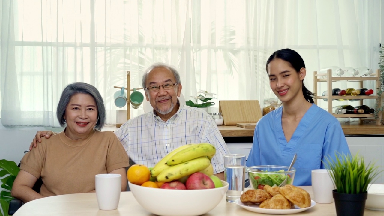 放大的亚裔老年祖父母和家庭护理护士正坐在餐桌上，有很多食物。视频下载