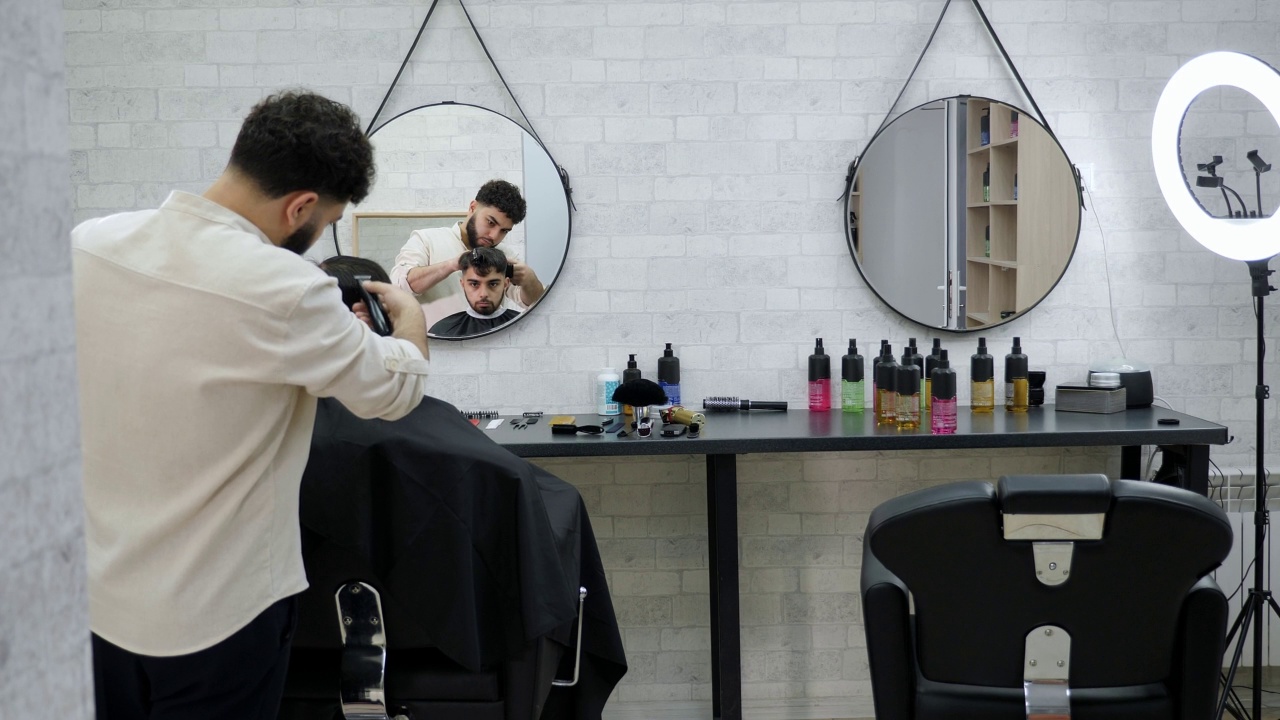 一位年轻的男理发师在一家现代化的理发店里和一位男顾客一起工作。视频素材