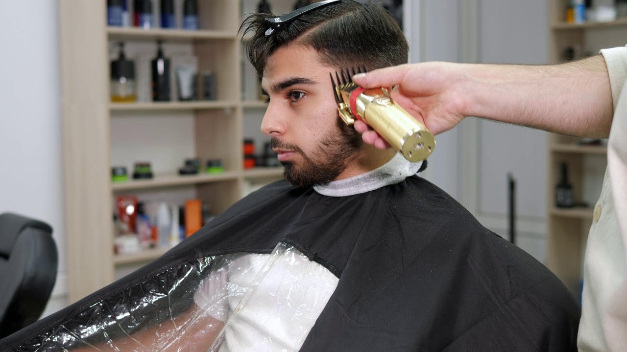 一个理发师用电动剃刀给一个黑发男人理发的特写。视频素材