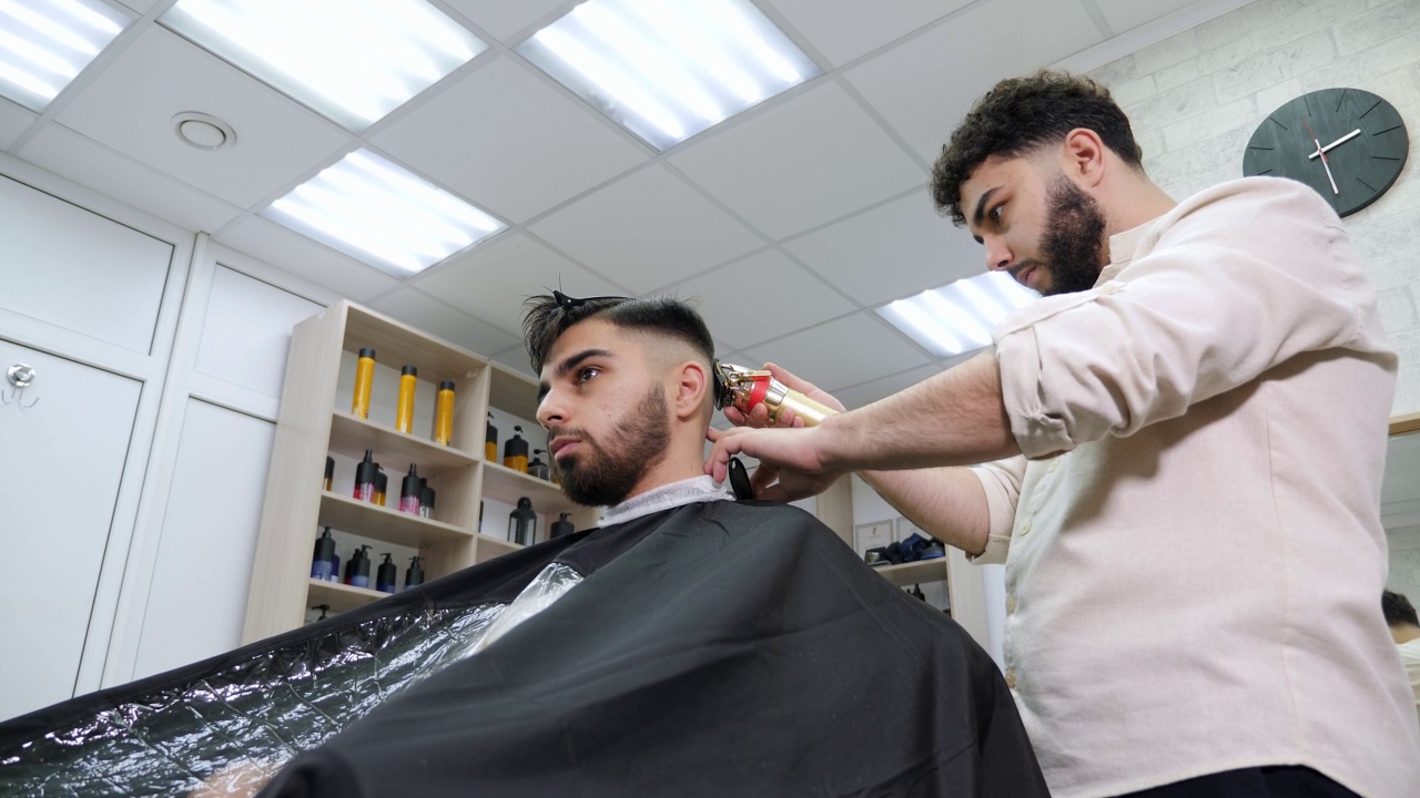 理发师用电动剃刀给顾客理发。视频素材