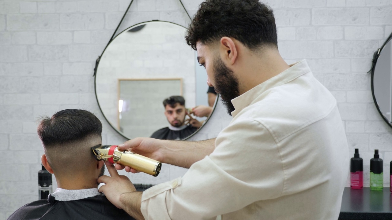 在现代理发店里，理发师用电动剃刀为顾客理发。视频素材