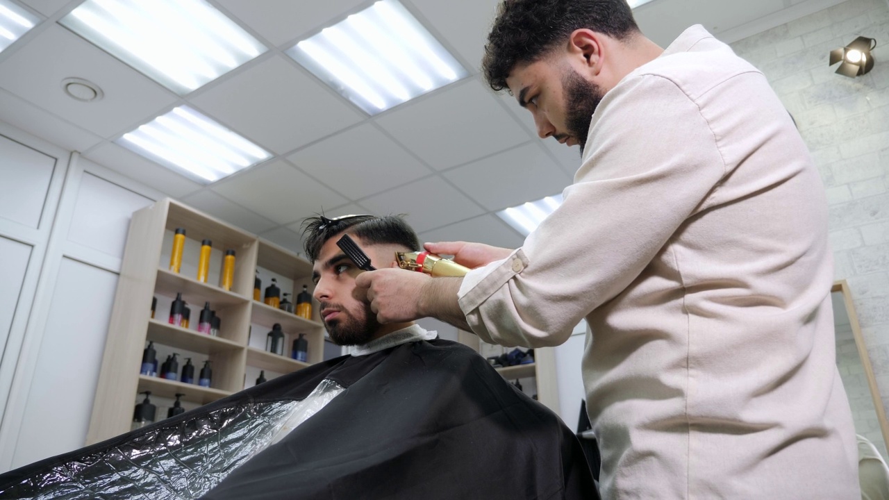 理发师用电动剪子给一个黑发男人剪头发。视频素材