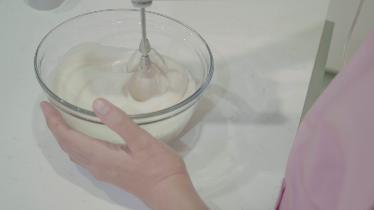 一位女士用电动手搅拌机在碗里混合蛋糕原料视频下载