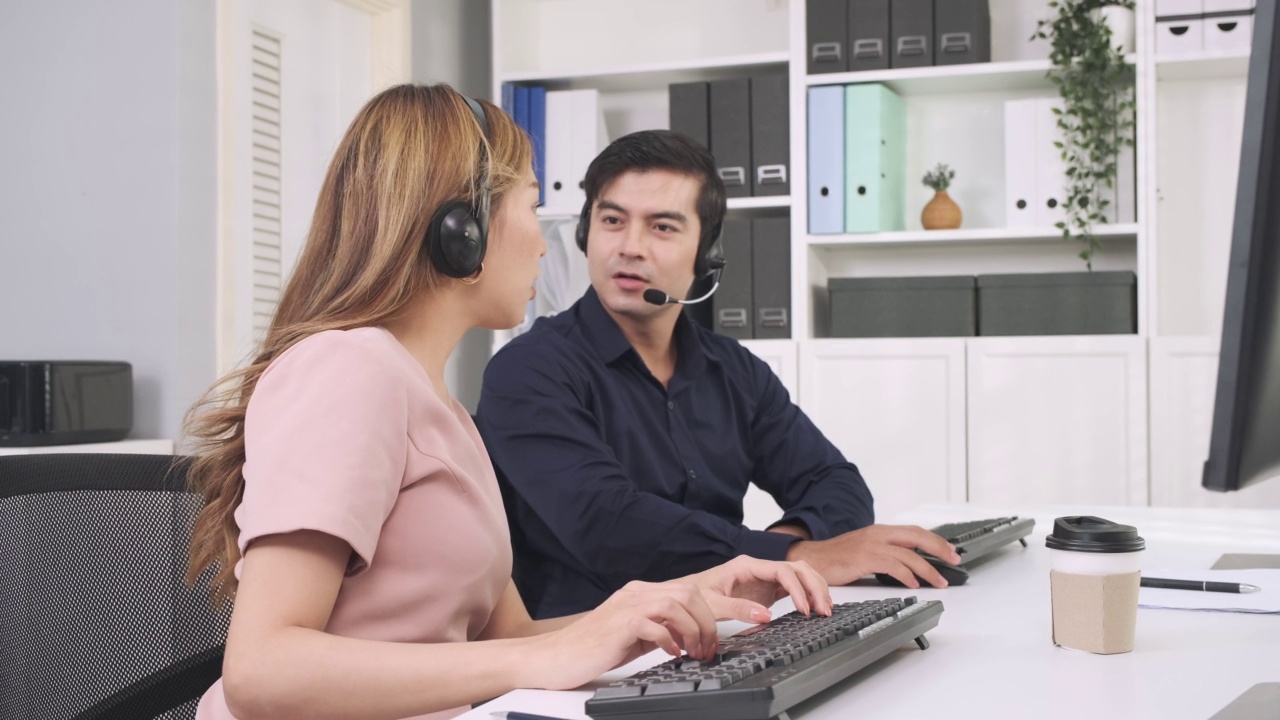 年轻的亚洲妇女戴着耳机在中心办公室的呼叫中心业务支持服务。视频素材