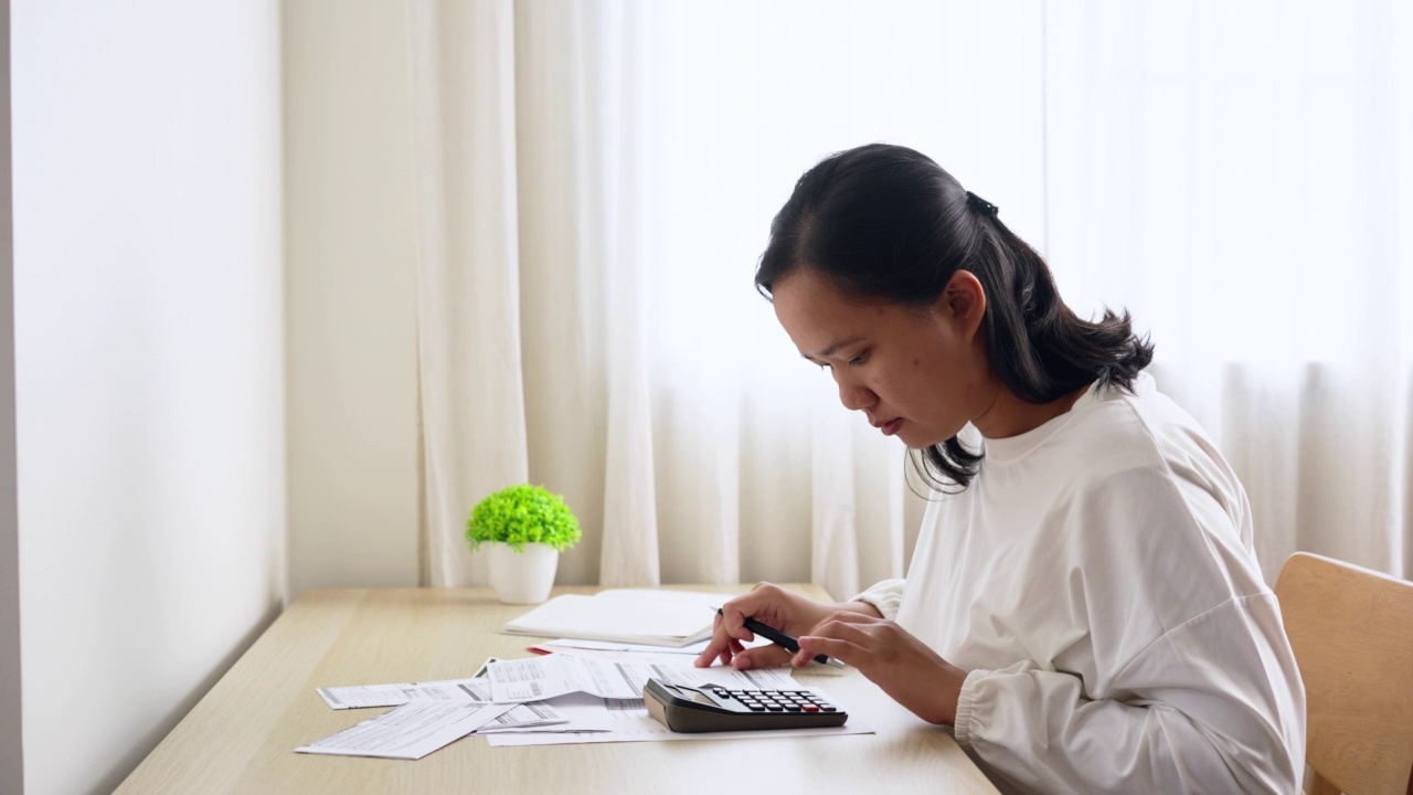 家庭财务规划与管理。年轻的亚洲妇女在家里计算家庭财务账单视频素材