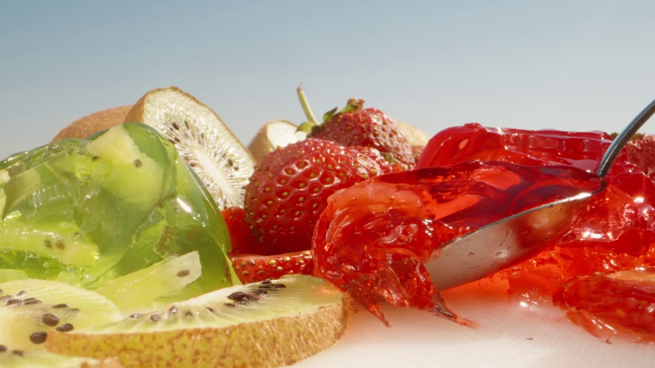 绿色和红色的果冻配草莓和猕猴桃，我吃了一勺草莓果冻。特写镜头。视频下载