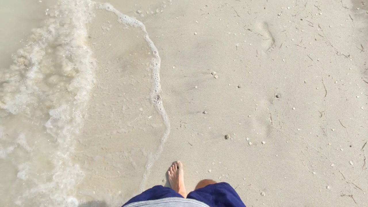 一个男人在阳光明媚的日子里走在沙滩上的视角视频素材