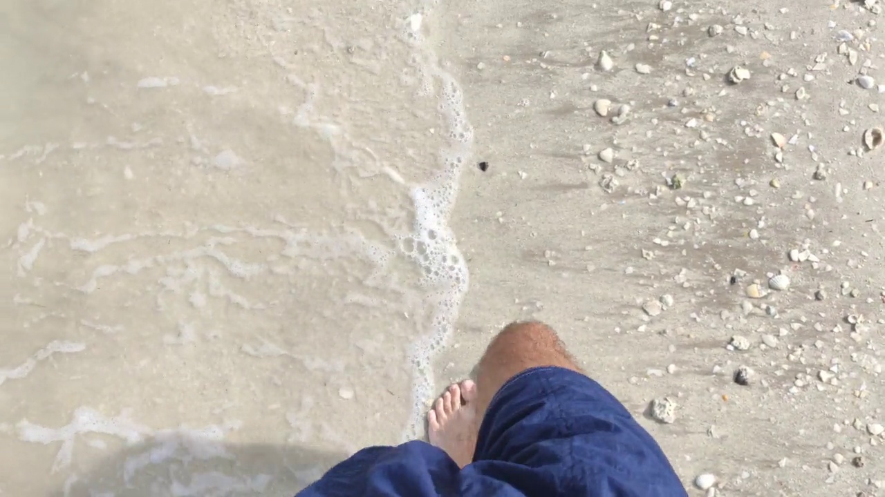 一个男人在阳光明媚的日子里走在沙滩上的视角视频素材