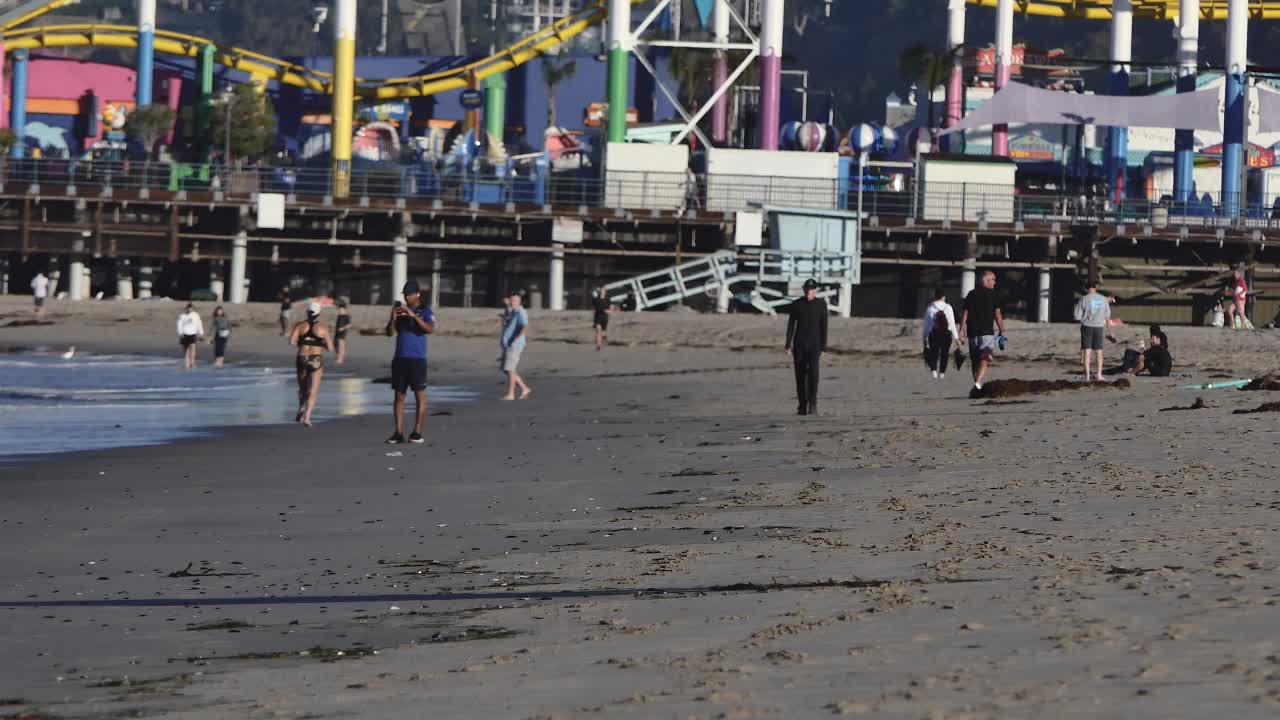 海滩上的人们，背景是游乐园视频下载