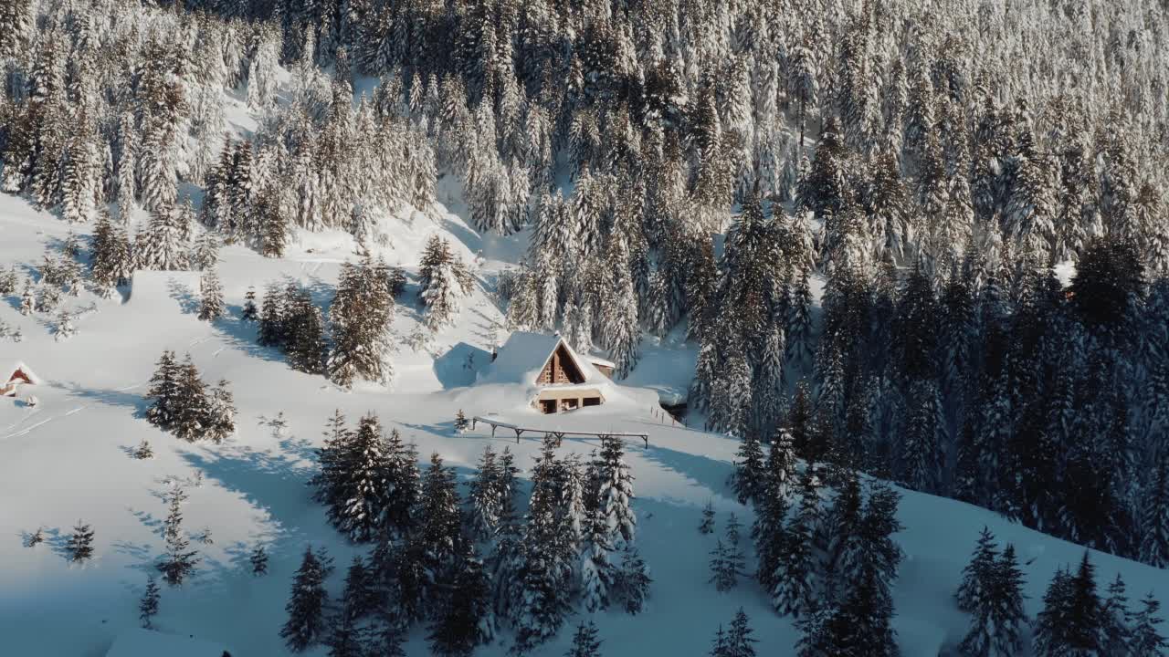 在一个阳光明媚的冬日早晨，无人机拍摄了一座覆盖着积雪的小农舍。遥远森林里的冬天童话。视频素材
