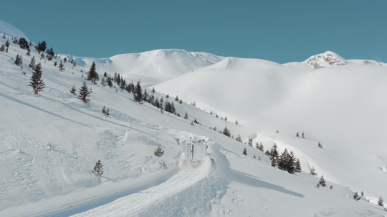 鸟瞰图雪猫拉架与雪犁准备道路滑雪者，和滑雪板在高海拔的山顶在一个阳光明媚的冬天。开车穿过滑雪场的深雪道，带着新鲜的粉。重型机械山地设备。视频素材