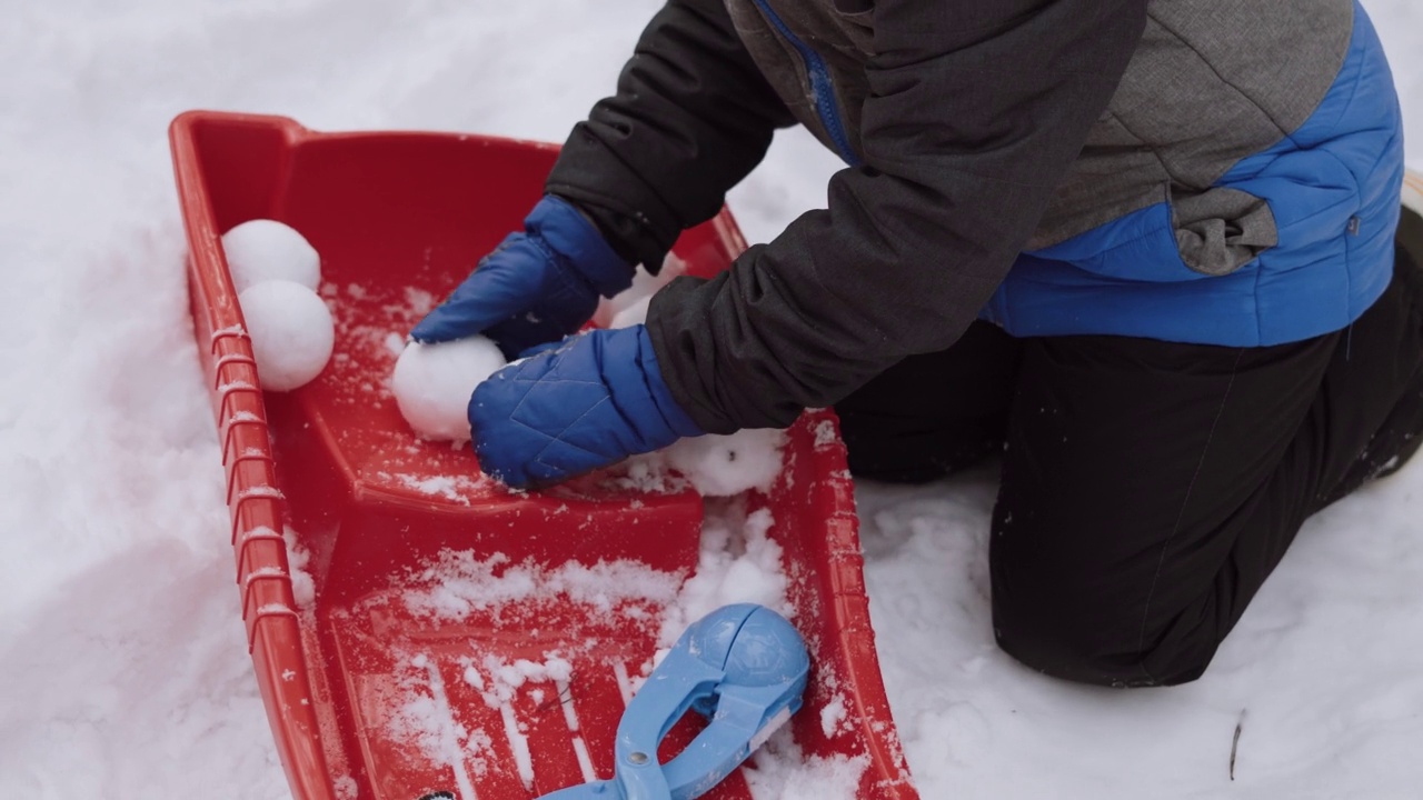 戴着连指手套的孩子在红色雪橇上放圆雪球，特写。视频下载