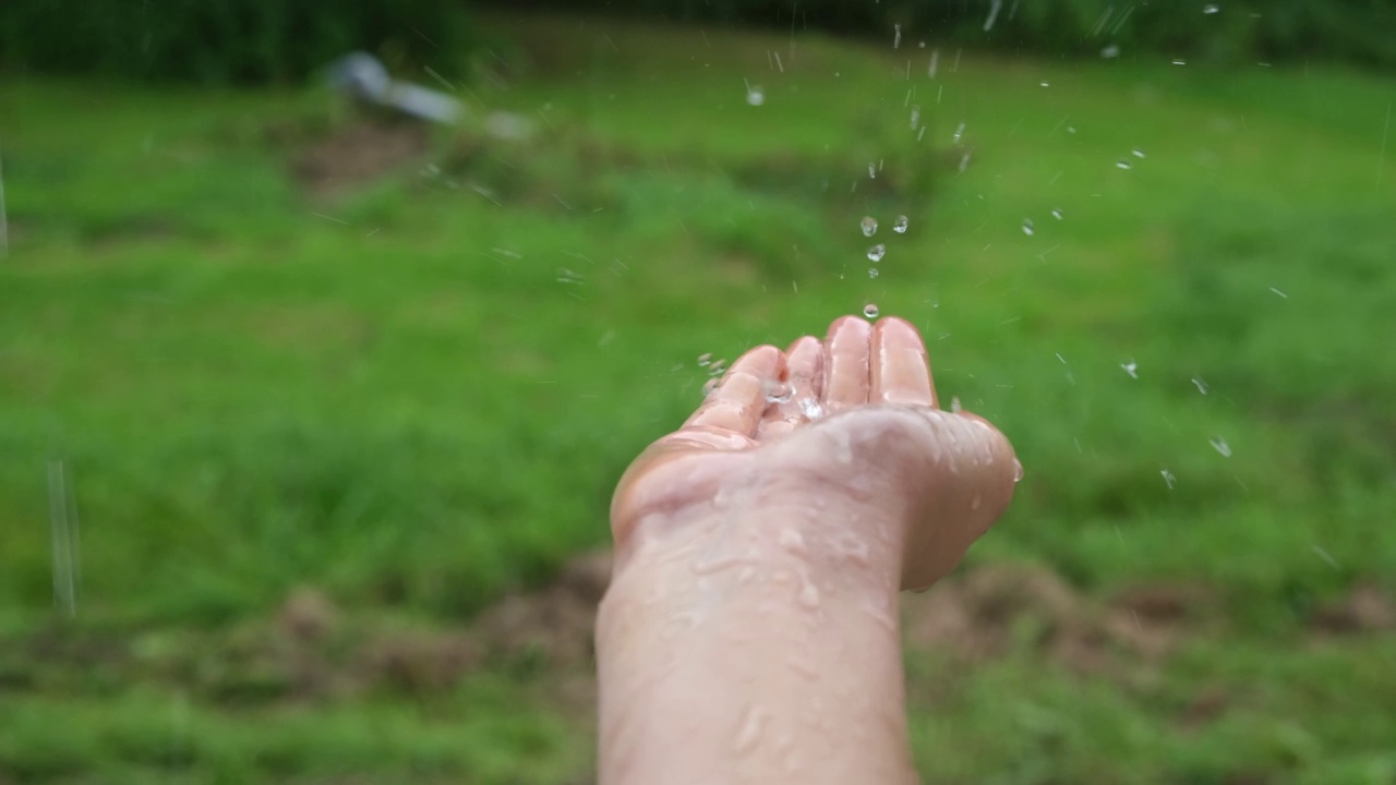 雨水落在少女的手上，背景是绿色的自然。环境恢复。女人在夏雨中享受着，握着她的手。大雨。特写镜头。森林里的雨天。多雨的天气视频素材