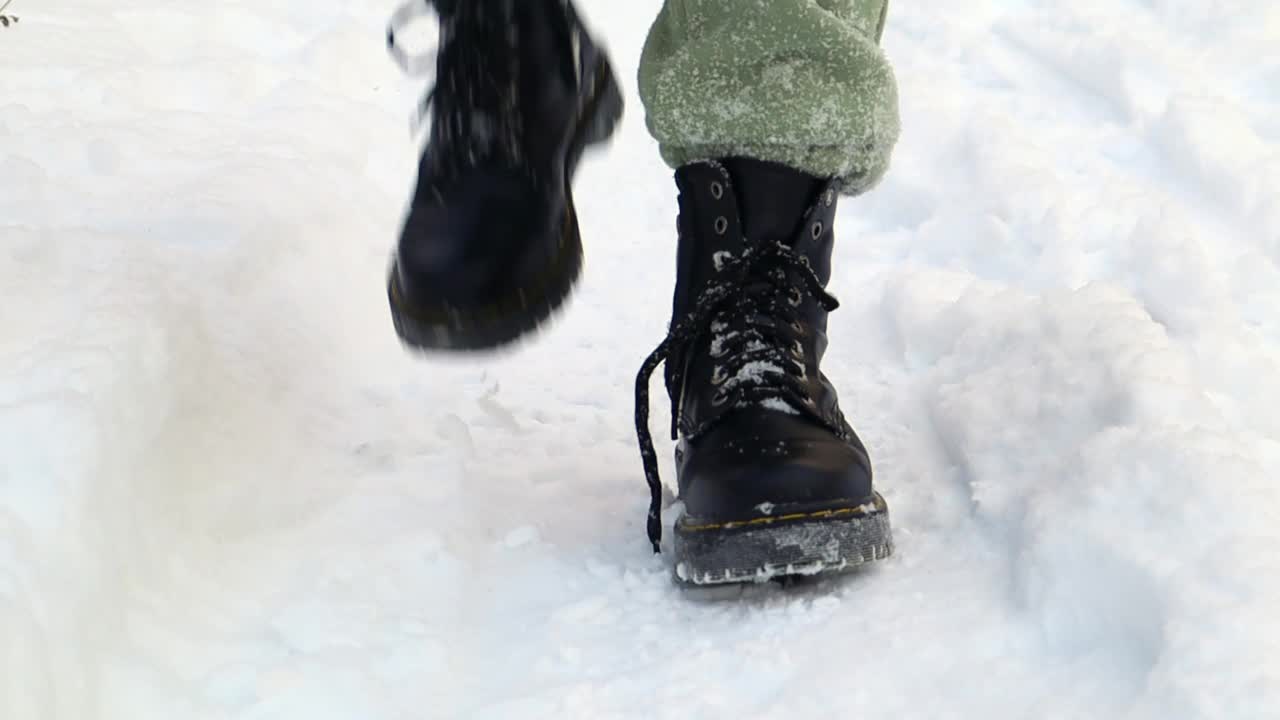 在冬天，一个穿着黑靴子的冻人站在那里。冬天，房子入口处靴子上的雪晃动的延时照片。抖掉鞋子上的雪，冬天下大雪。视频下载