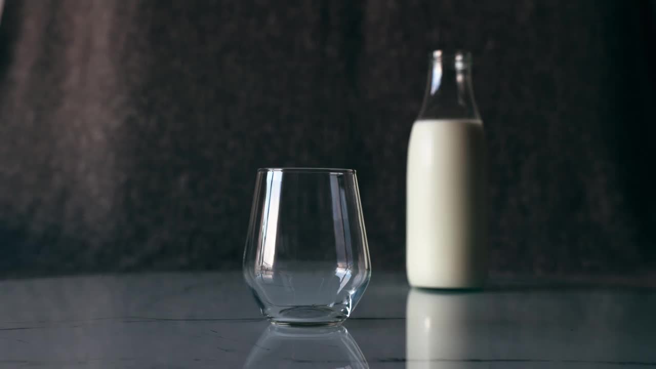盛满一瓶的白牛奶倒进桌上的玻璃杯里。视频素材