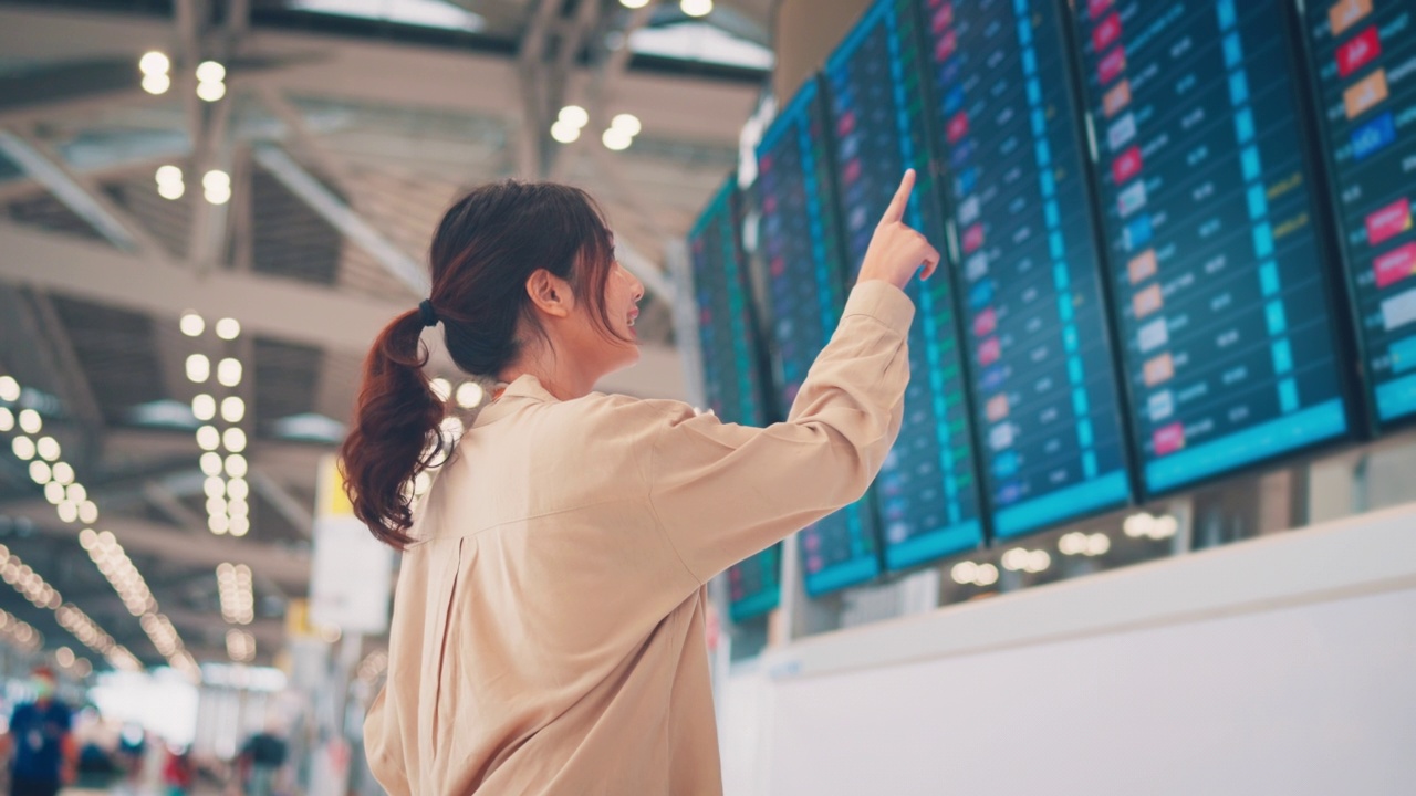 快乐的亚洲女旅客在机场候机楼查看航班时刻表。旅游旅程旅行概念视频素材