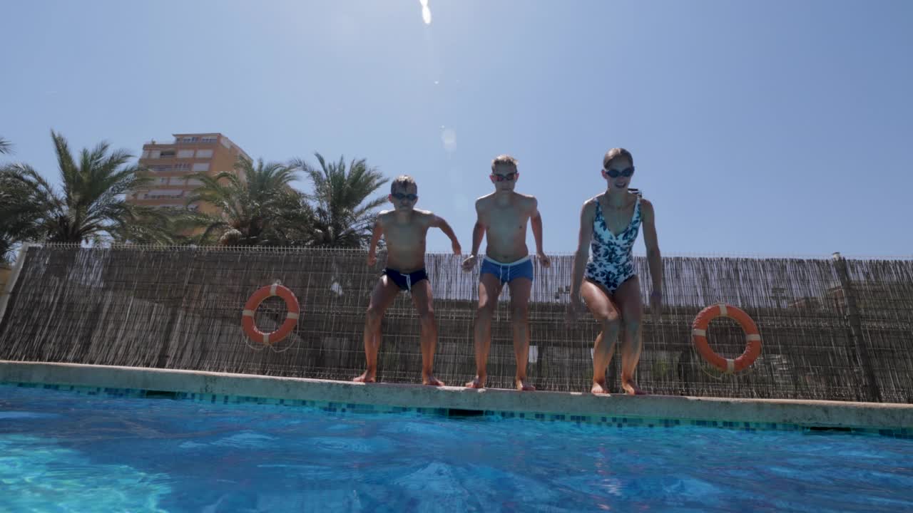在一个阳光明媚的夏日，三个快乐的十几岁的孩子跳入游泳池。视频素材