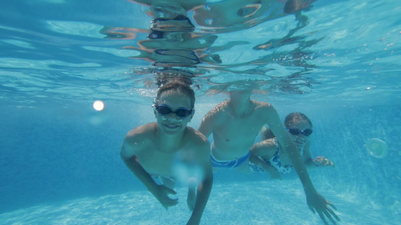在一个阳光明媚的夏天，三个快乐的十几岁的孩子在游泳池里游泳。视频素材