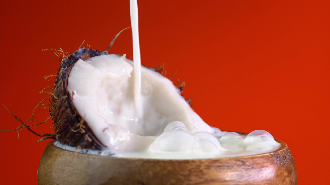 倒椰奶，滴椰子水，椰子油滴在红色的背景上。新鲜的椰子碎和飞溅的牛奶。做水果鸡尾酒，喝冰柠檬水视频下载