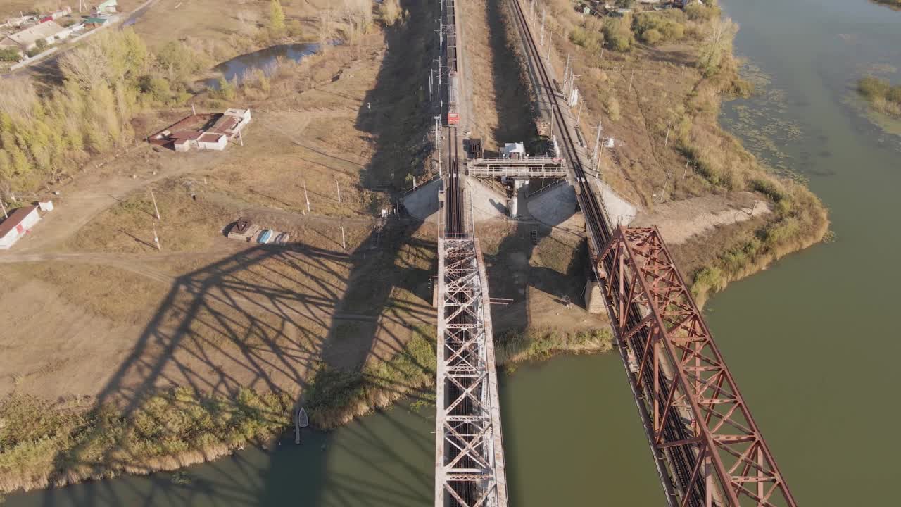 一辆载着煤的货车的电力机车在河上的铁路桥上通过铁路行驶。用马车运输和交付货物铁路运输和物流。视频下载
