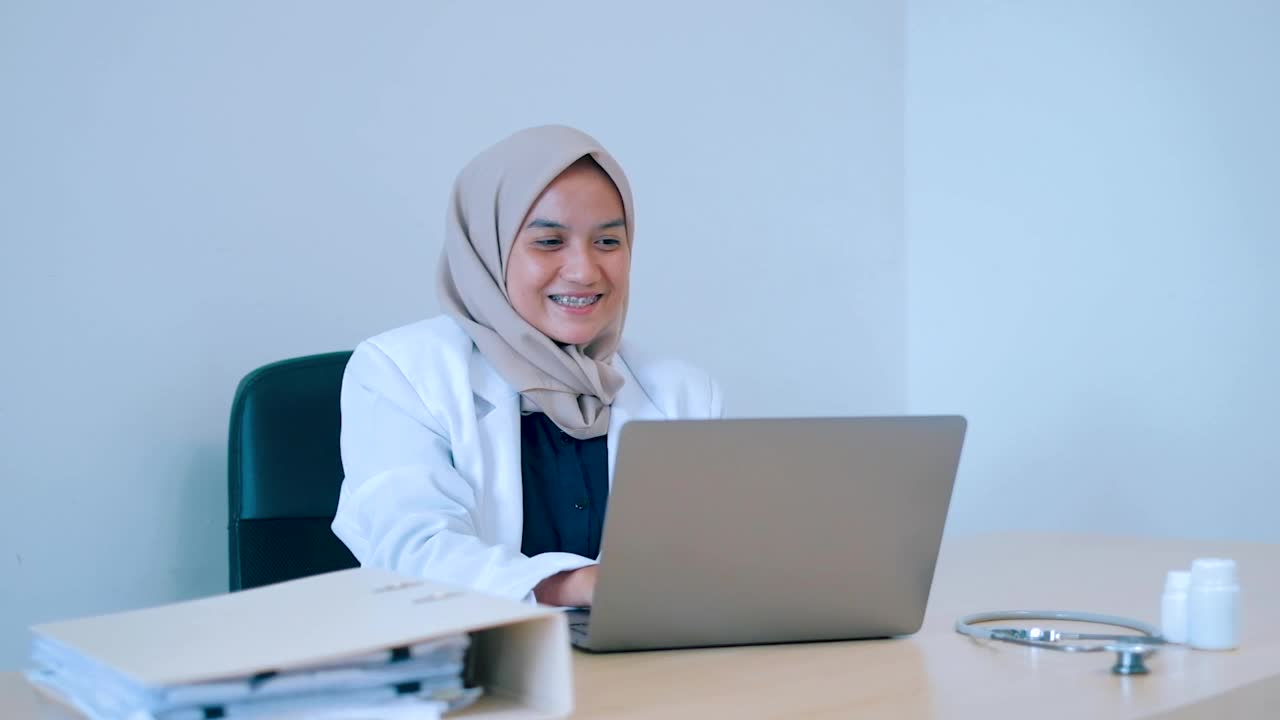 快乐的亚洲女医生工作与笔记本电脑在办公室的桌子上。视频素材