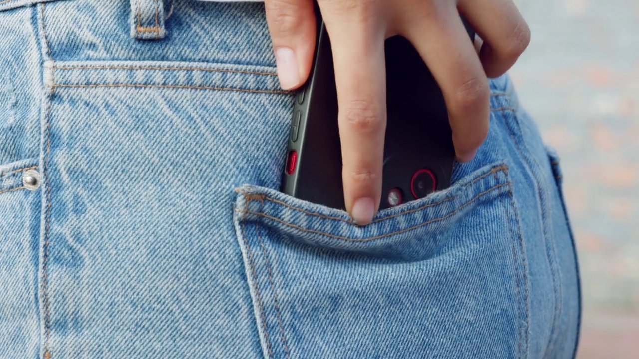 手，手机和牛仔裤，一个女人把手机放在外面的牛仔裤口袋里。手机，时尚和交流，一个女人把她的智能手机放在裤子后面的口袋在户外视频下载