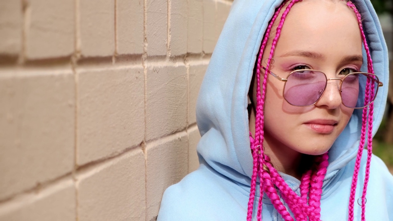 肖像的白人少女潮女孩粉红色的辫子对着粉红色的砖墙。Z一代的风格。视频下载