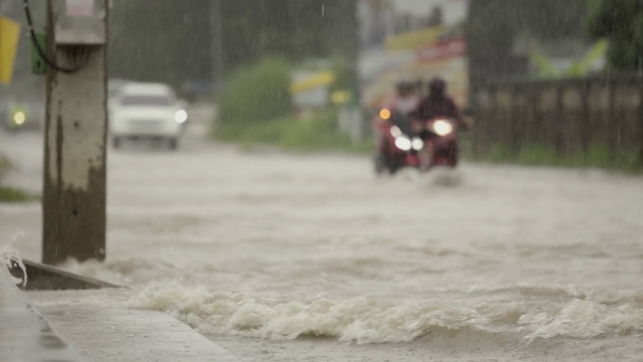 在暴雨引发的洪水中行驶在被淹道路上的汽车。雨下着，汽车跑在满是水的路上。视频素材