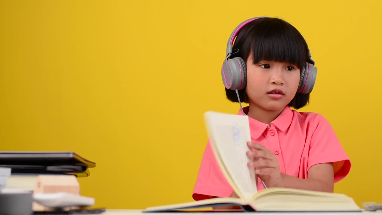 可爱的小女孩在他家里的桌子上一边看书一边听着放松的音乐。视频下载