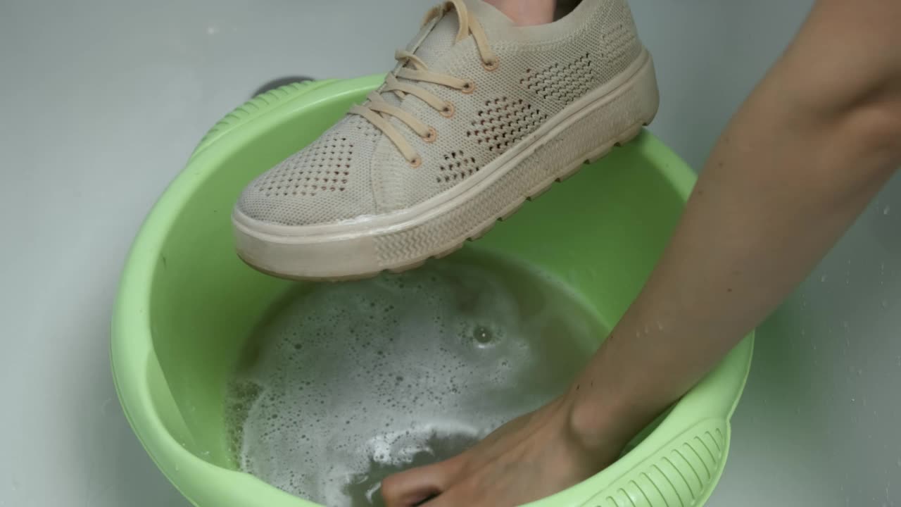女子正在用海绵用手在盆里洗运动鞋，特写手。视频素材