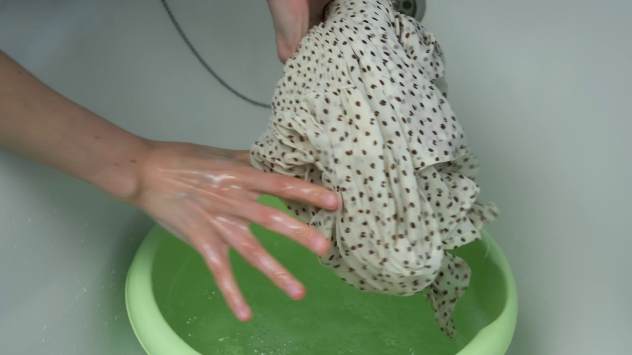 一个女人在盆上拧干一件手洗的衣服，近景。视频素材