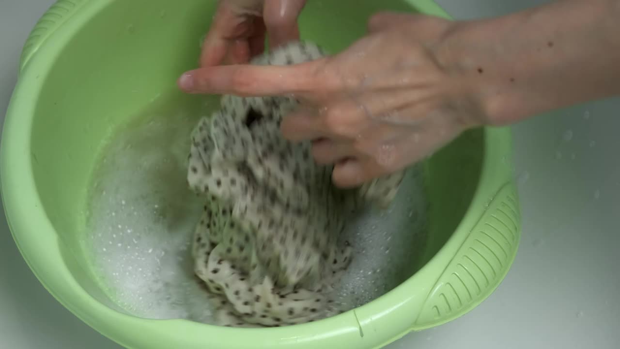妇女正在用手在肥皂水里洗洗精致面料上的衣服。视频素材