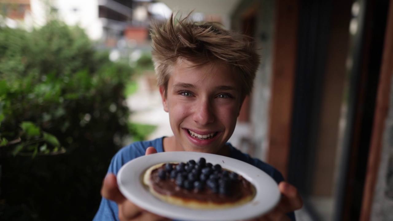 十几岁的男孩拿着一盘煎饼上面有巧克力和蓝莓视频素材