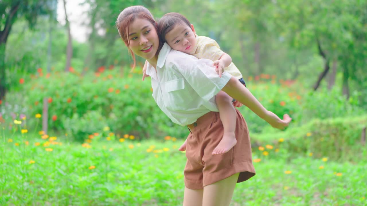 亚洲母亲抱着她的儿子在公园或花园晨光中快乐地玩耍。视频素材