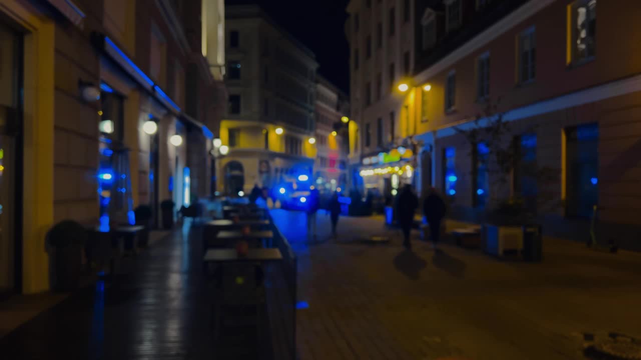 离焦:人们在夜晚的城市中行走，撞向一辆警笛闪烁的救护车视频素材