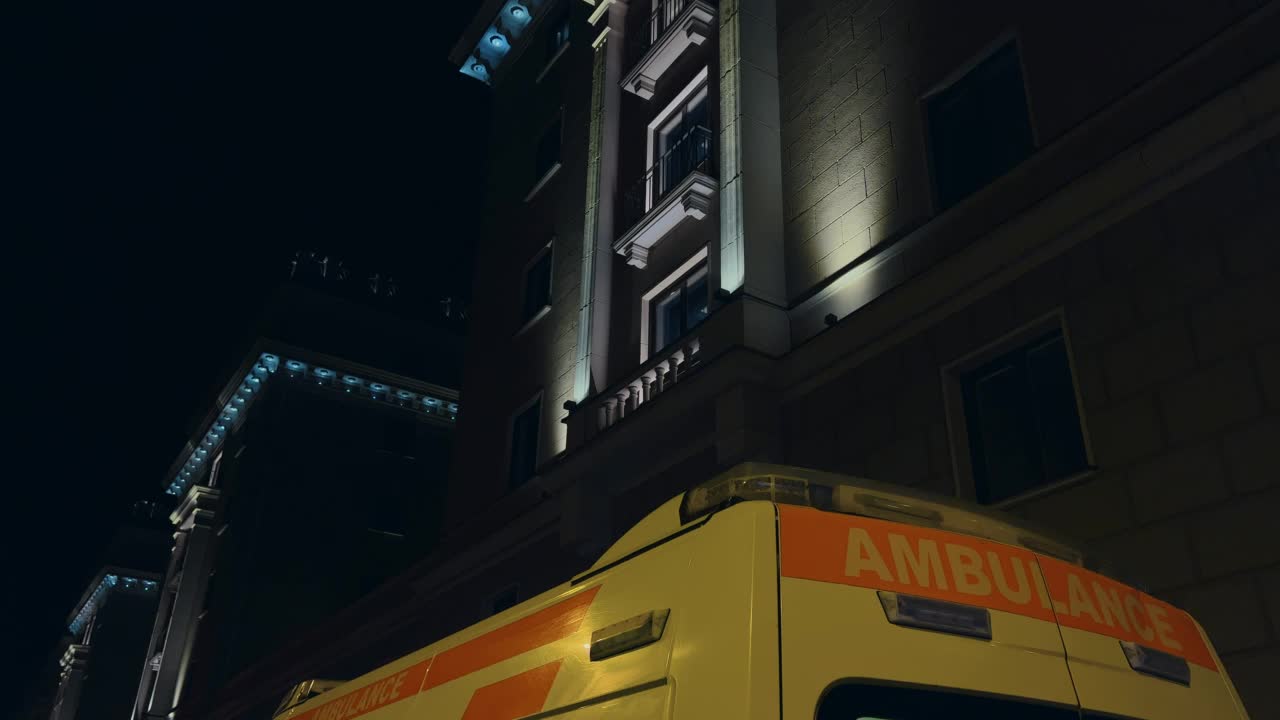 夜晚:黄色救护车撞在巨大的酒店大楼上，警笛闪烁视频素材