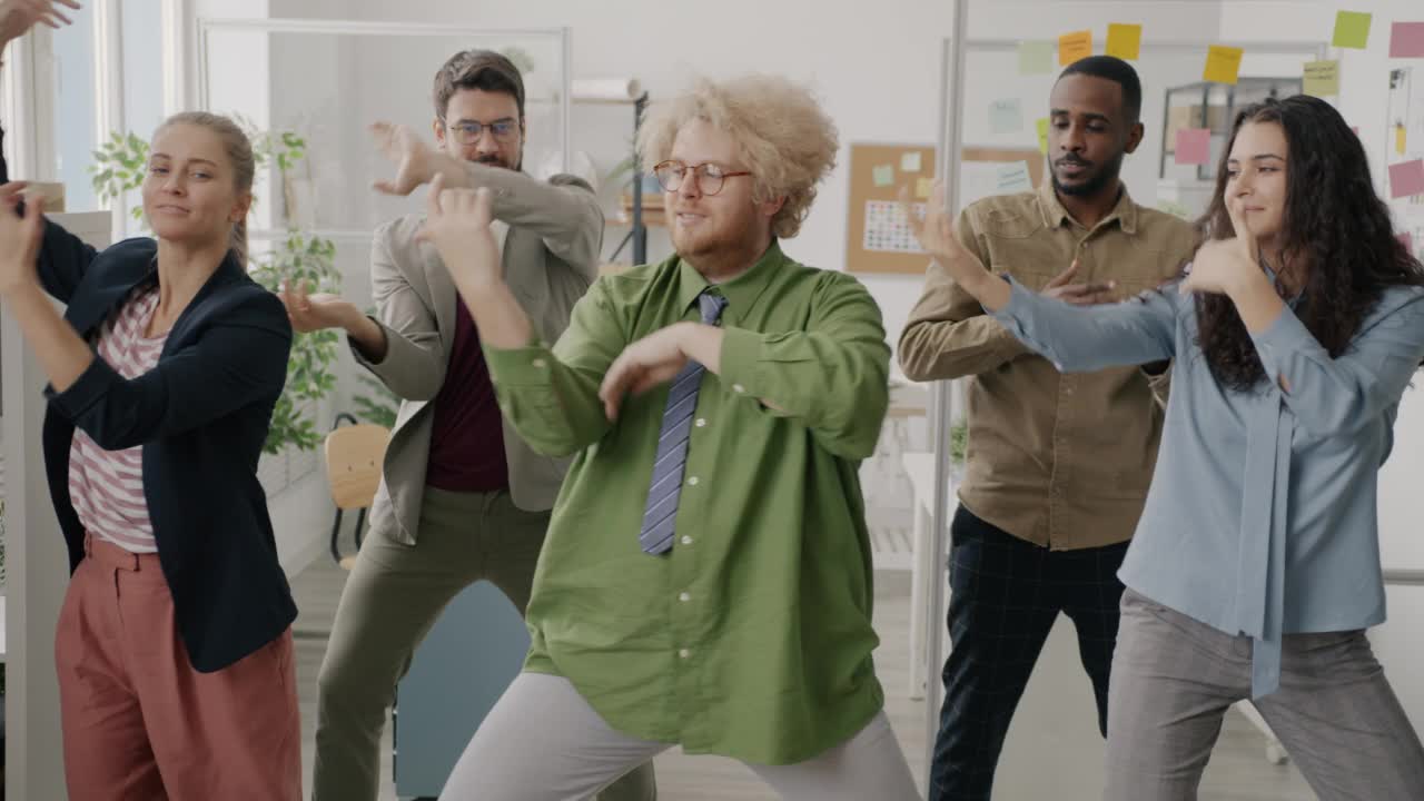 疯狂的年轻员工在办公室跳舞，舞动着手臂，微笑着，在工作中玩得很开心视频素材