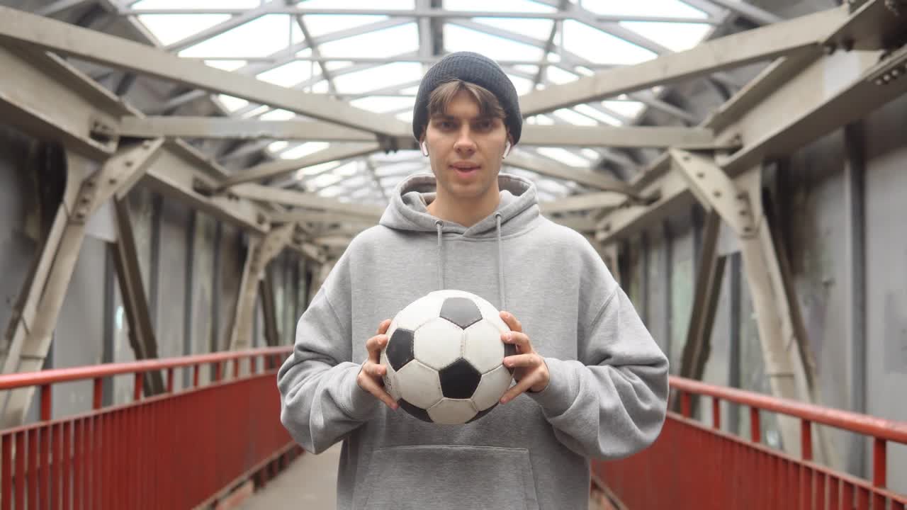 年轻的潮人拿着足球在城市背景。积极生活方式的概念。视频购买