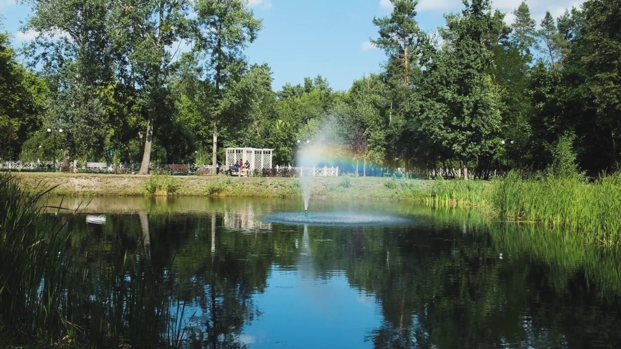 在一个晴朗的日子里，一个城市池塘中央的工作喷泉，背景是一个带孩子的家庭，一个公园里绿树成荫的总体规划视频下载