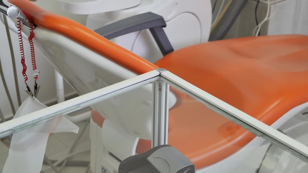 戴着蓝色手套的牙科助理把一套牙科器械放在橙色牙科椅旁边的玻璃桌上，供牙医在治疗病人时使用。视频素材