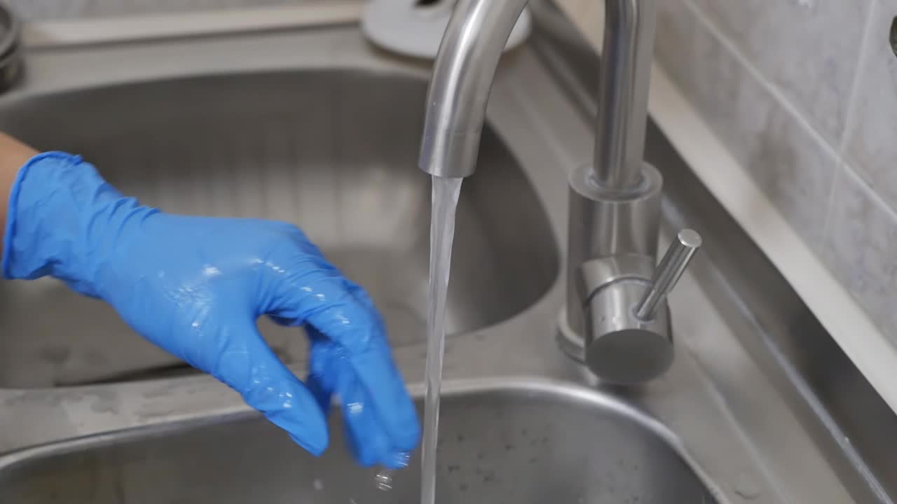 戴着蓝色手套的医护人员用泡沫清洁剂和海绵在自来水中清洗医疗手术器械的双手特写。医疗器械灭菌过程视频素材