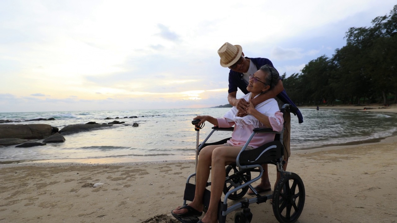 男长者在假日和假期照顾坐在轮椅上的妻子。退休和放松的概念。视频下载