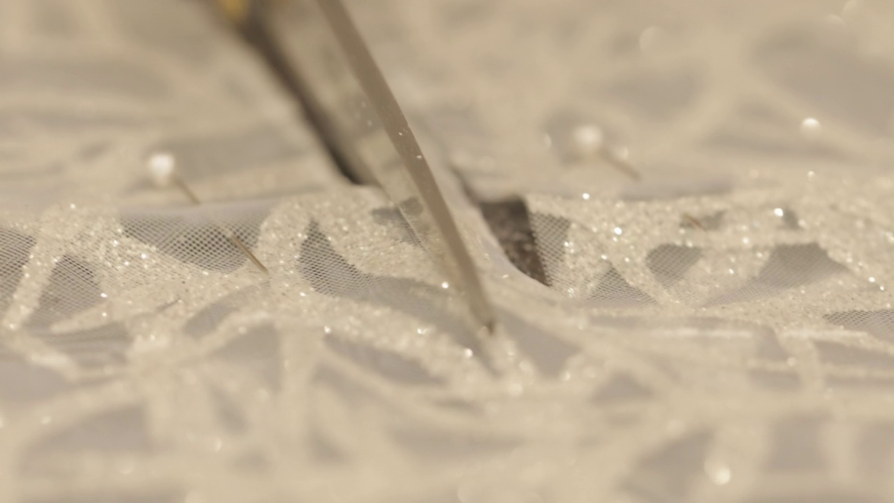 在制作婚纱的过程中，剪刀剪开了白色闪亮的布料。宏观视图视频下载
