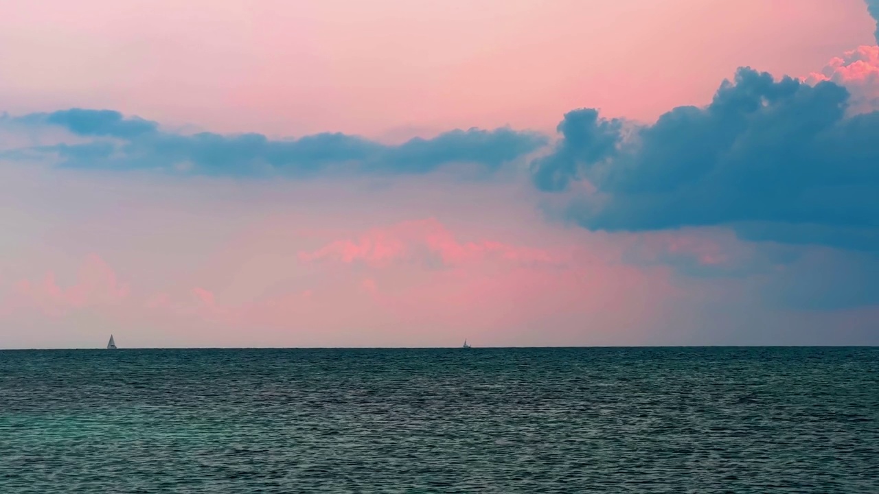 远处的帆船在日落时航行在地平线上，上面是粉红色的多云的天空和波光粼粼的海面视频素材