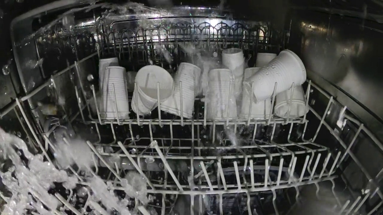 塑料盘子在洗碗机里洗。疯狂的想法是用洗碗机洗塑料玻璃。查看内部洗碗机和一次性塑料餐具。慢动作内部视图。视频下载
