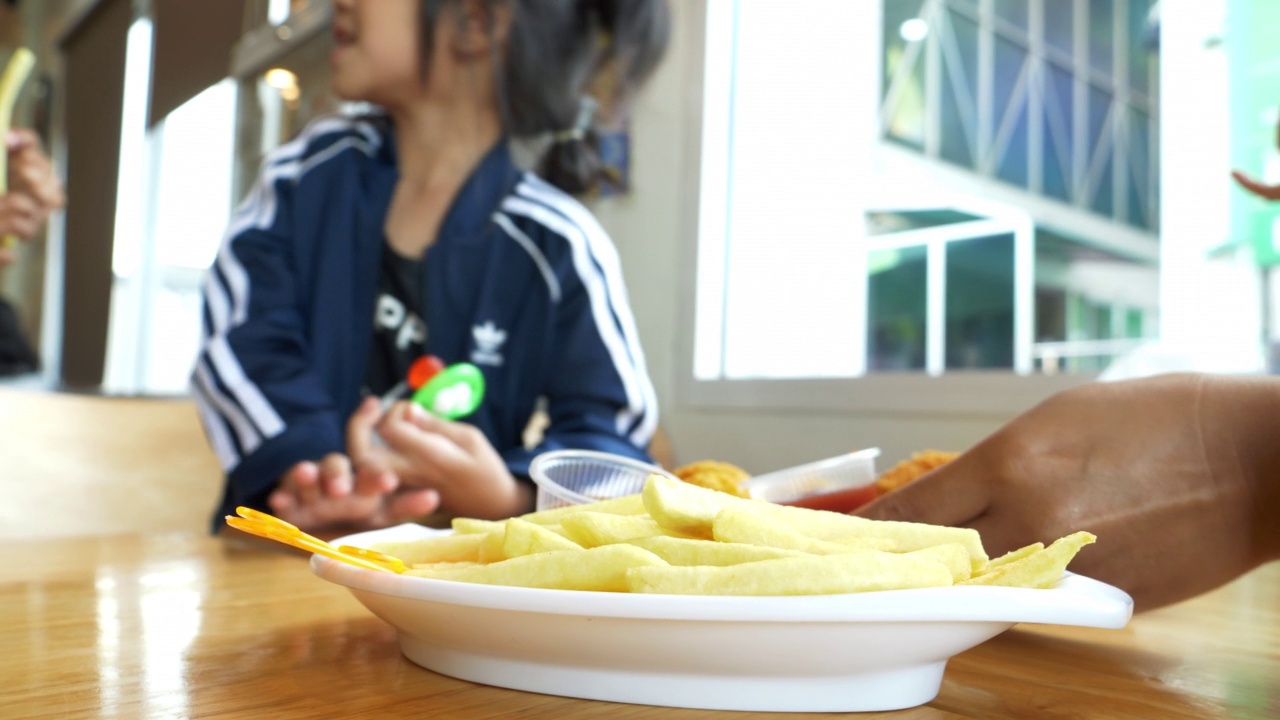 孩子用手拣着桌上白色盘子里的薯条。视频素材
