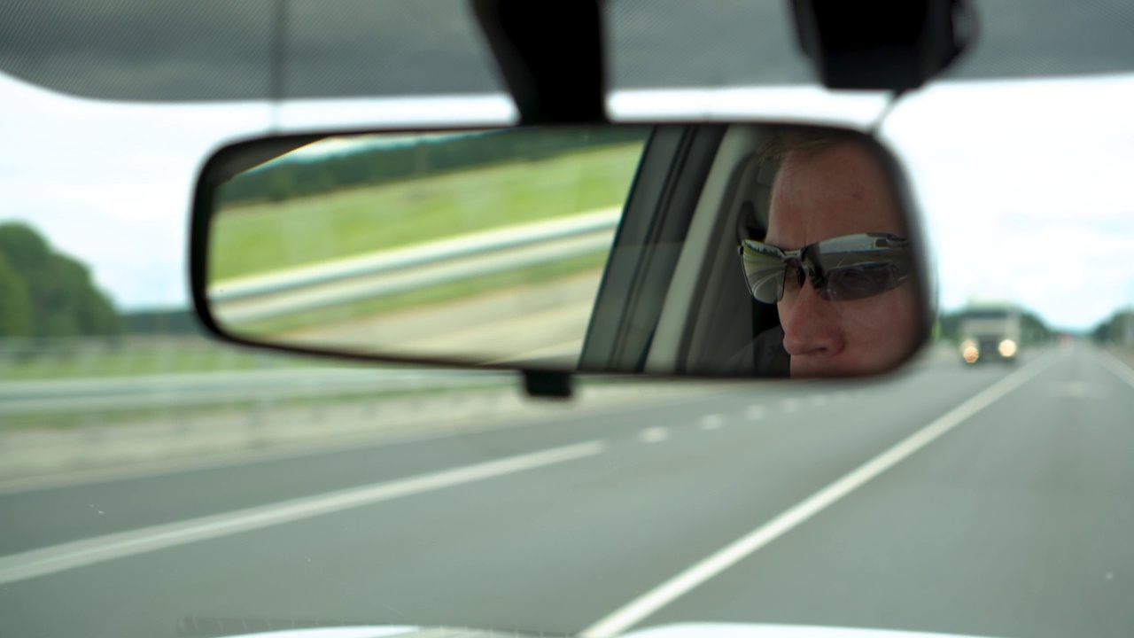 在俄罗斯，一名白人男子在高速公路上开车，从后视镜中可以看到视频下载