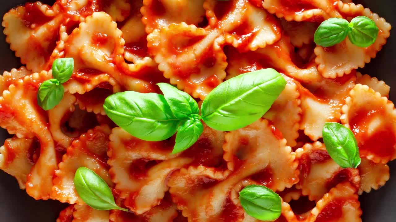 法尔法尔，近景微距，用番茄酱和罗勒绿叶烹饪的意大利面，俯视图，循环旋转。视频下载