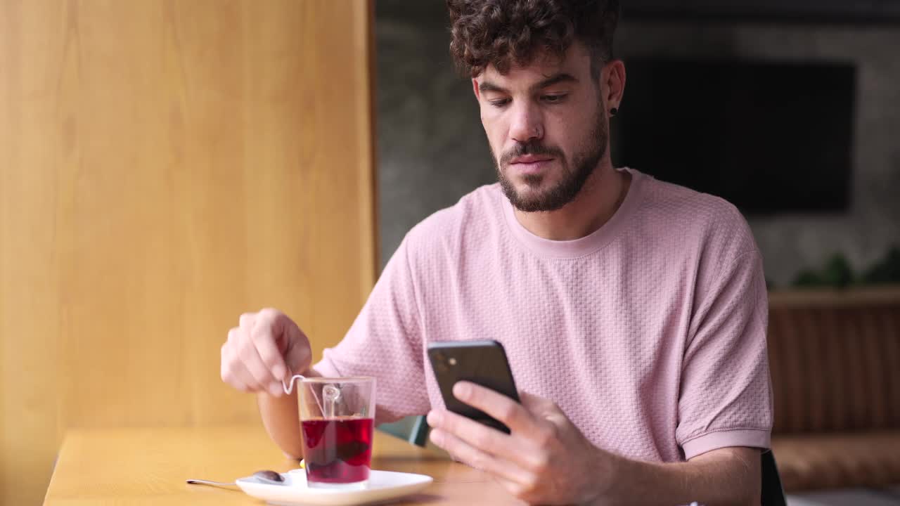 一个年轻人在咖啡馆里喝茶，用手机。视频素材